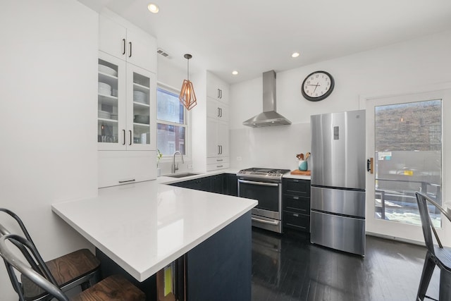 kitchen with appliances with stainless steel finishes, a kitchen breakfast bar, wall chimney range hood, sink, and kitchen peninsula