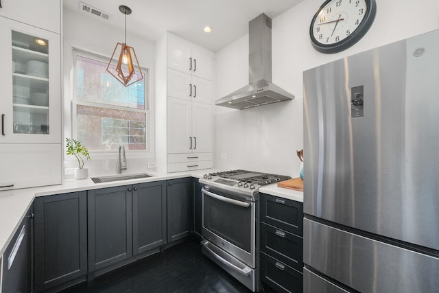 kitchen with appliances with stainless steel finishes, sink, wall chimney exhaust hood, white cabinets, and hanging light fixtures