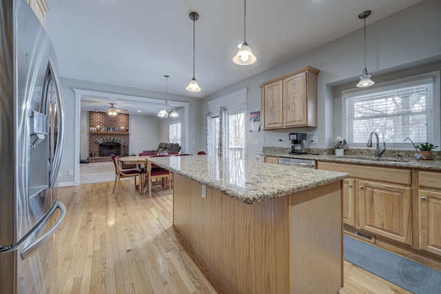 kitchen featuring light brown cabinetry, stainless steel appliances, decorative light fixtures, a center island, and sink