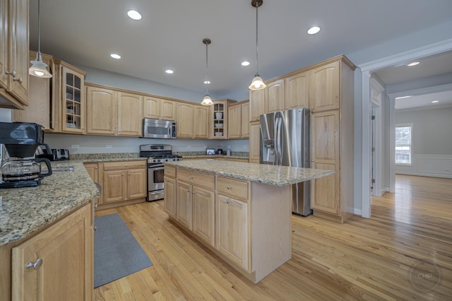 kitchen featuring appliances with stainless steel finishes, a kitchen island, hanging light fixtures, and light stone counters