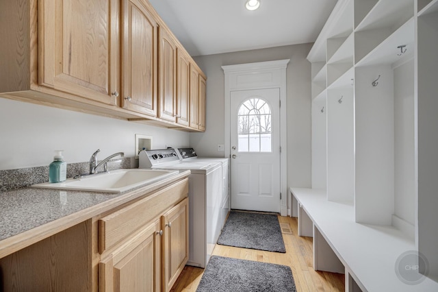 laundry room with washing machine and clothes dryer, sink, cabinets, and light hardwood / wood-style flooring