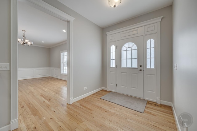 foyer entrance with ornamental molding, an inviting chandelier, and light hardwood / wood-style floors