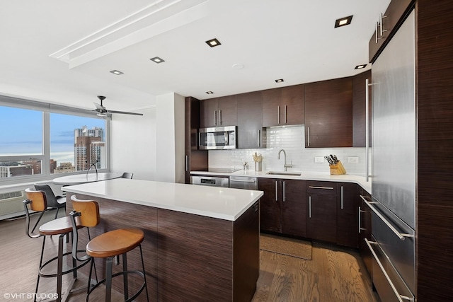 kitchen with appliances with stainless steel finishes, a kitchen breakfast bar, wood finished floors, light countertops, and a sink