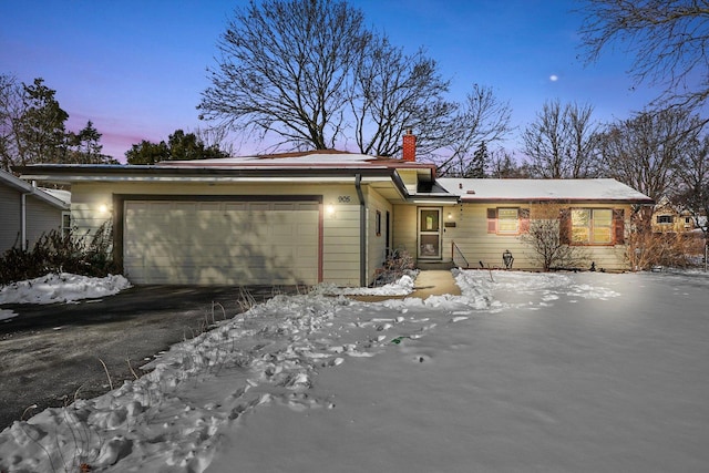 ranch-style home featuring a chimney, aphalt driveway, and a garage