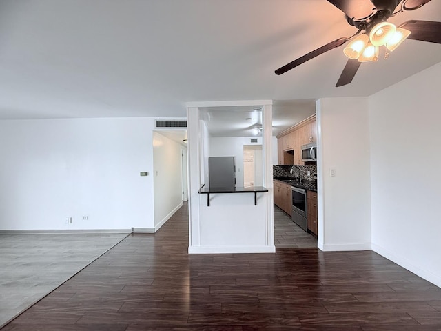 kitchen with dark wood-type flooring, appliances with stainless steel finishes, tasteful backsplash, and ceiling fan