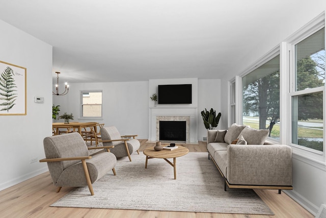 living room featuring light wood-style flooring, a fireplace with flush hearth, visible vents, baseboards, and an inviting chandelier