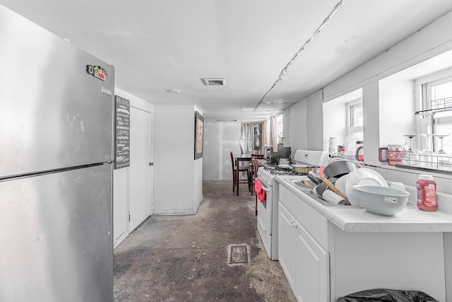 kitchen with stainless steel refrigerator, white cabinets, and white range with gas stovetop