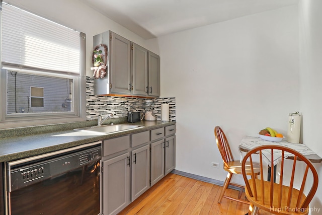 kitchen featuring black dishwasher, dark countertops, decorative backsplash, gray cabinetry, and a sink