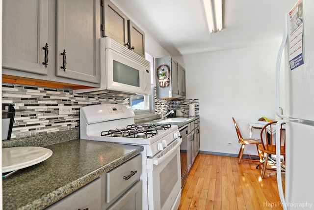 kitchen featuring tasteful backsplash, white appliances, a sink, and gray cabinetry