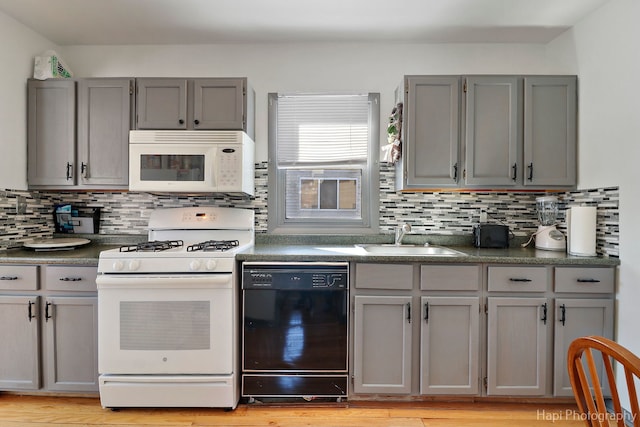 kitchen featuring dark countertops, white appliances, a sink, and gray cabinetry