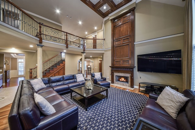 living room with wood-type flooring, decorative columns, a high end fireplace, a high ceiling, and beam ceiling