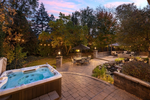 pool at dusk featuring a patio and an outdoor hot tub