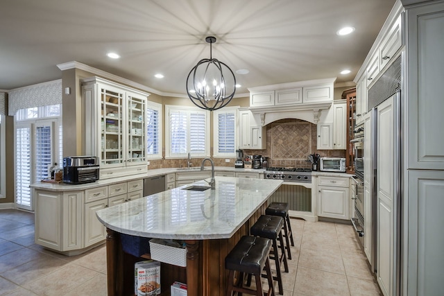 kitchen featuring light stone countertops, stainless steel dishwasher, decorative light fixtures, light tile patterned floors, and a kitchen island with sink