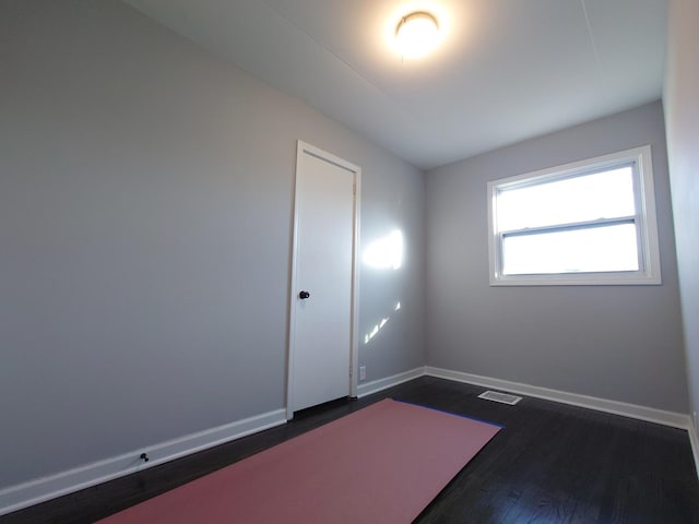 spare room with dark wood-style flooring, visible vents, and baseboards