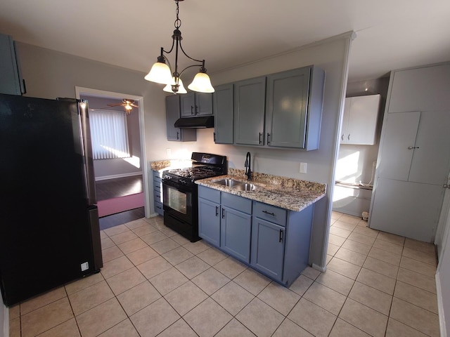 kitchen with light tile patterned floors, black gas range, under cabinet range hood, a sink, and freestanding refrigerator