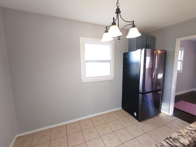 kitchen featuring light tile patterned floors, plenty of natural light, freestanding refrigerator, and baseboards