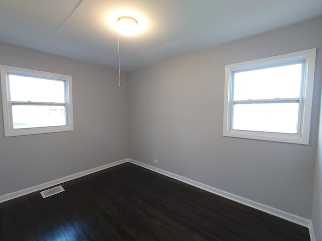 unfurnished room with dark wood-type flooring, a healthy amount of sunlight, visible vents, and baseboards