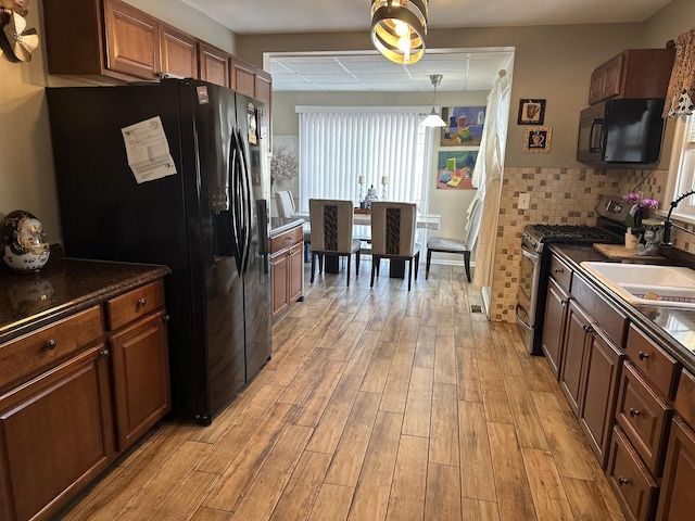 kitchen with decorative light fixtures, black appliances, light hardwood / wood-style floors, sink, and backsplash