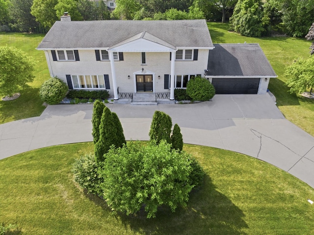 greek revival house featuring a front yard, driveway, a chimney, a garage, and brick siding