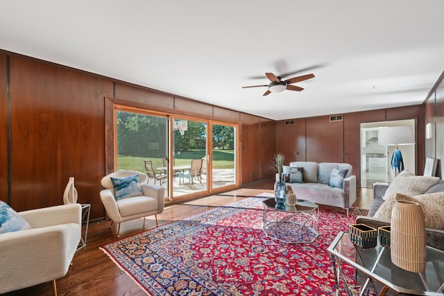 living area featuring wood finished floors, visible vents, wood walls, and ceiling fan