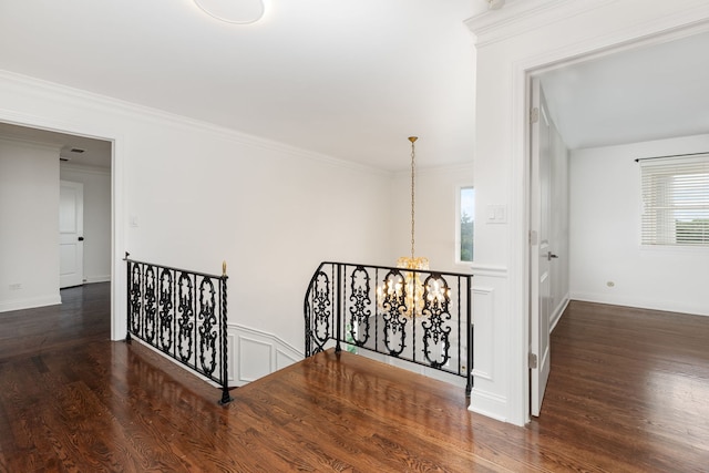 corridor featuring an upstairs landing, an inviting chandelier, wood finished floors, and ornamental molding