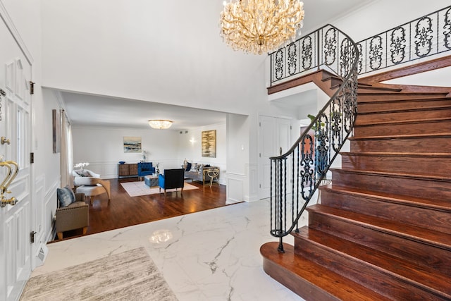 entrance foyer featuring crown molding, stairway, wainscoting, a decorative wall, and marble finish floor