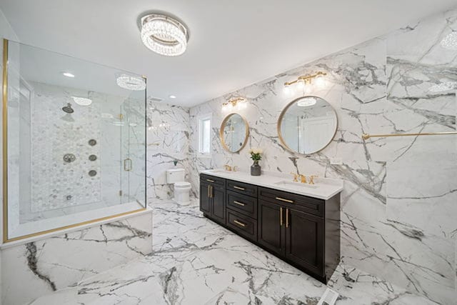 full bath featuring stone wall, toilet, marble finish floor, a marble finish shower, and double vanity