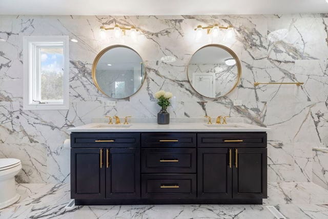 bathroom featuring double vanity, stone wall, toilet, and a sink