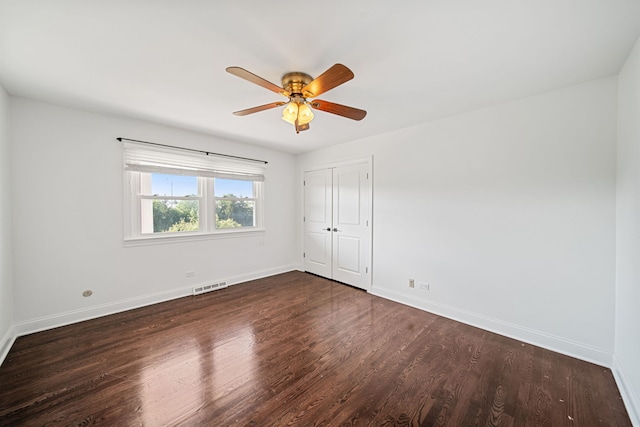 unfurnished room featuring baseboards, visible vents, dark wood finished floors, and a ceiling fan