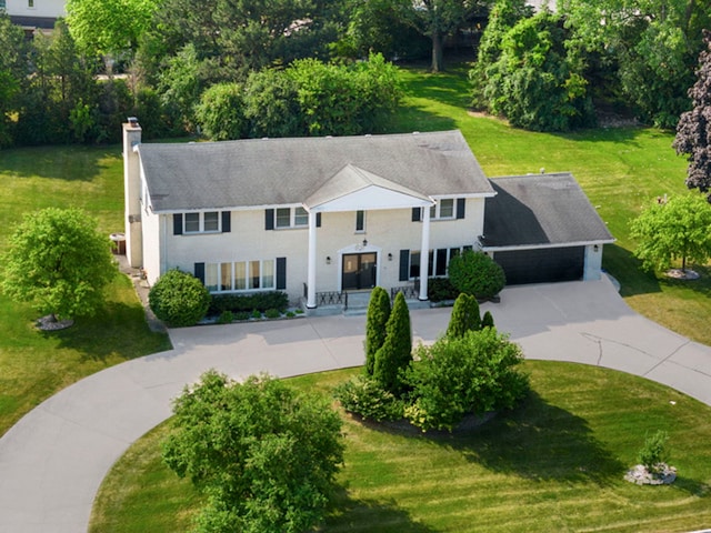 view of front of house featuring a front yard, driveway, a chimney, and an attached garage