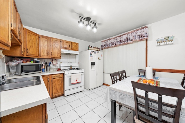 kitchen with under cabinet range hood, white appliances, a sink, light countertops, and brown cabinetry