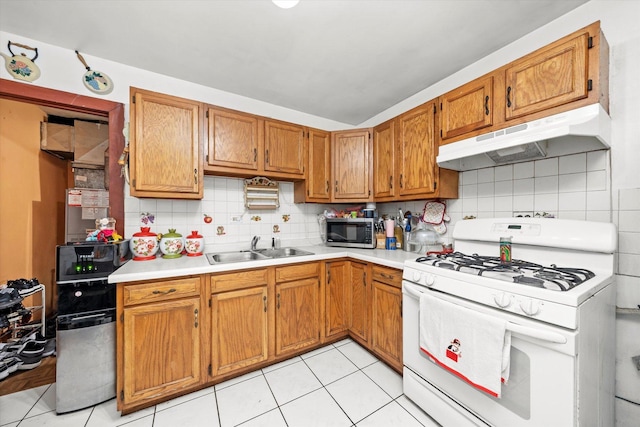 kitchen with light countertops, stainless steel microwave, a sink, white range with gas stovetop, and under cabinet range hood