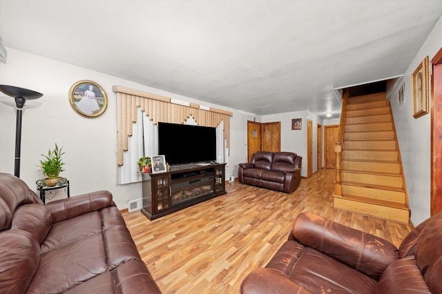 living room with stairs, light wood-style flooring, and visible vents