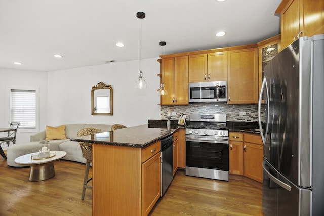 kitchen with appliances with stainless steel finishes, pendant lighting, kitchen peninsula, a kitchen bar, and dark stone countertops