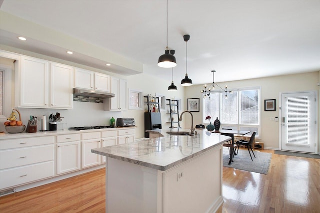 kitchen featuring an inviting chandelier, a sink, white cabinets, under cabinet range hood, and light wood-type flooring