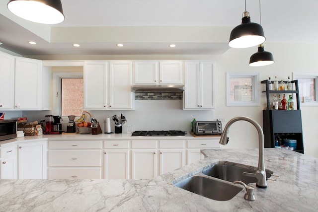 kitchen featuring black gas stovetop, a sink, stainless steel microwave, under cabinet range hood, and white cabinets