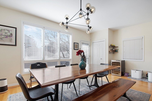 dining room featuring an inviting chandelier, beverage cooler, baseboards, and light wood finished floors