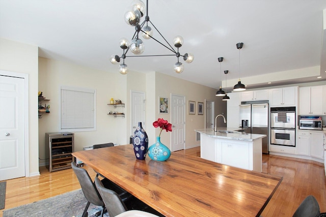 dining area featuring a chandelier, baseboards, light wood-style floors, and beverage cooler