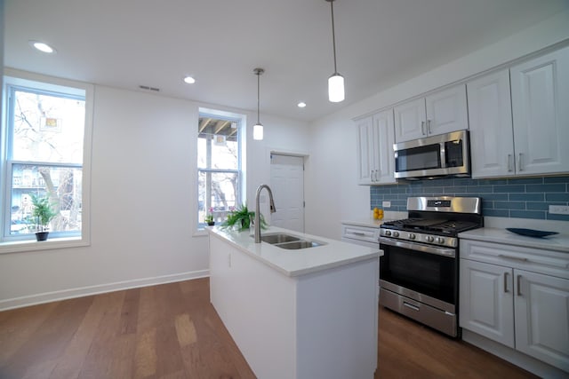 kitchen featuring stainless steel appliances, light countertops, white cabinets, a sink, and an island with sink