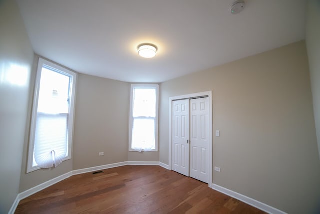 unfurnished bedroom with a closet, dark wood-style flooring, visible vents, and baseboards