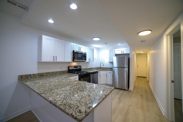 kitchen with stainless steel appliances, white cabinetry, a peninsula, and light stone countertops