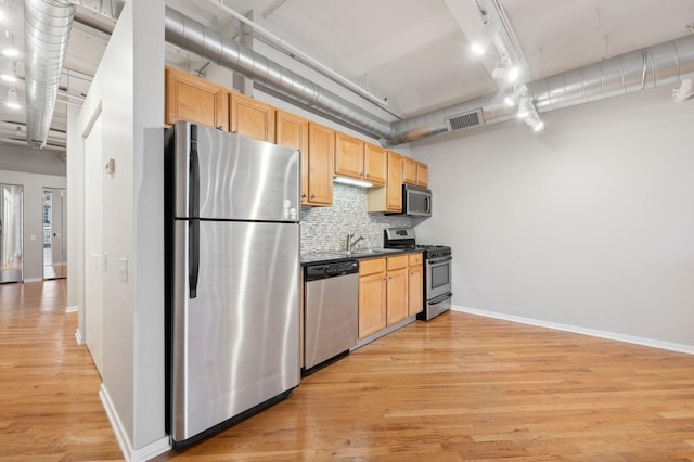 kitchen with light wood-type flooring, stainless steel appliances, backsplash, track lighting, and light brown cabinetry