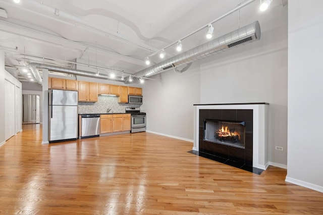 kitchen with light hardwood / wood-style floors, appliances with stainless steel finishes, a tiled fireplace, and decorative backsplash