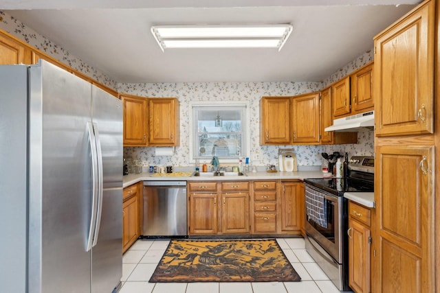 kitchen with under cabinet range hood, a sink, light countertops, appliances with stainless steel finishes, and wallpapered walls