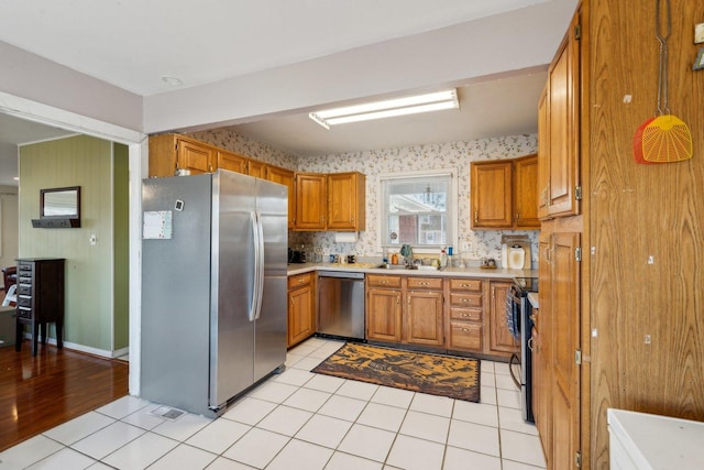 kitchen featuring light tile patterned flooring, stainless steel appliances, light countertops, brown cabinets, and wallpapered walls