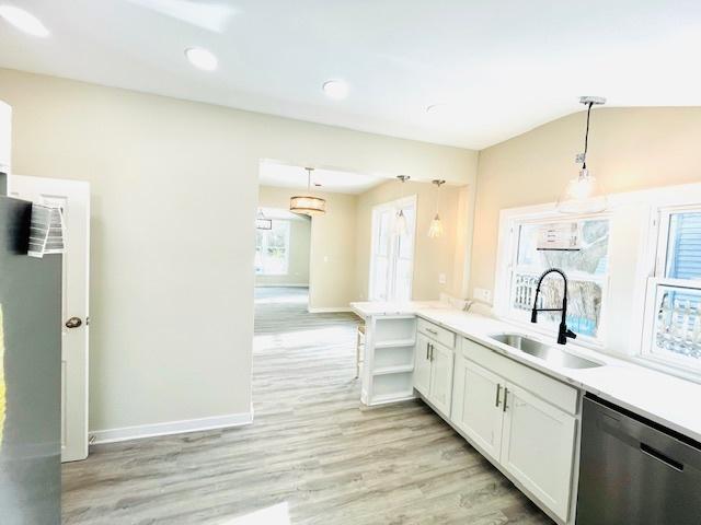 kitchen featuring hanging light fixtures, light countertops, stainless steel dishwasher, white cabinetry, and a sink