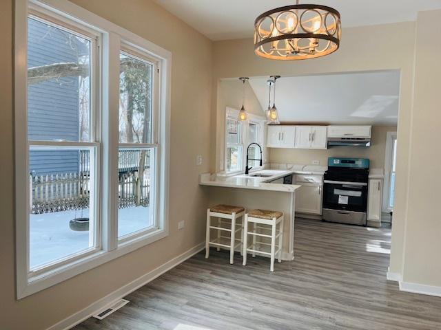 kitchen with stainless steel electric stove, white cabinets, light countertops, and decorative light fixtures