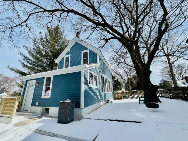 view of snowy exterior with a chimney, fence, and cooling unit