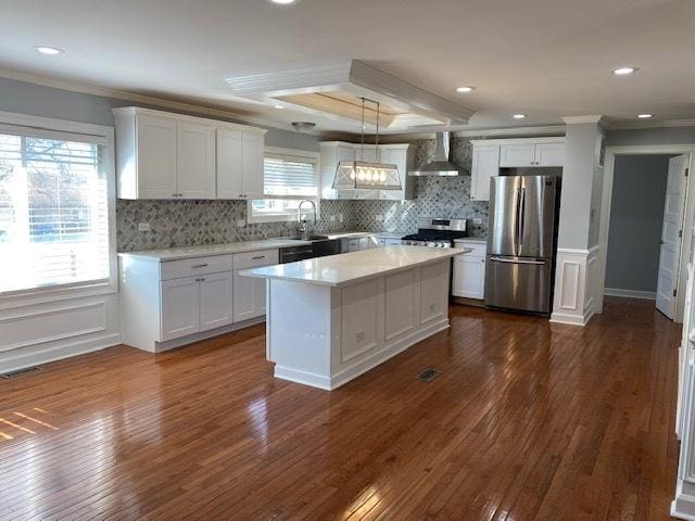 kitchen featuring white cabinetry, wall chimney range hood, stainless steel fridge, and pendant lighting