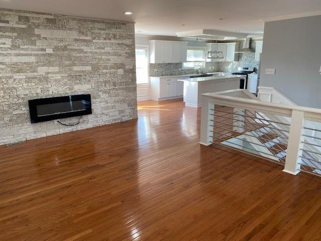 kitchen featuring a fireplace, hardwood / wood-style floors, tasteful backsplash, stainless steel range oven, and white cabinets